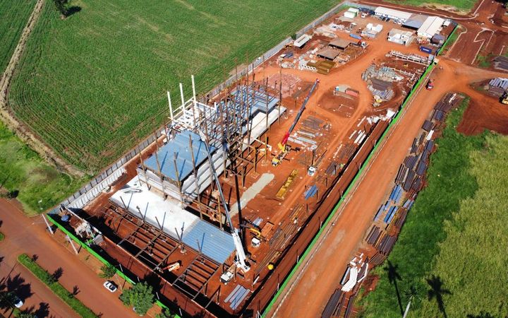 Canteiro visto de cima: estrutura metálica em montagem, terraplanagem e estoque de material